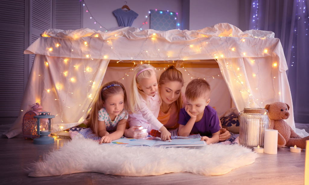 three children and their mother in a blanket fort reading