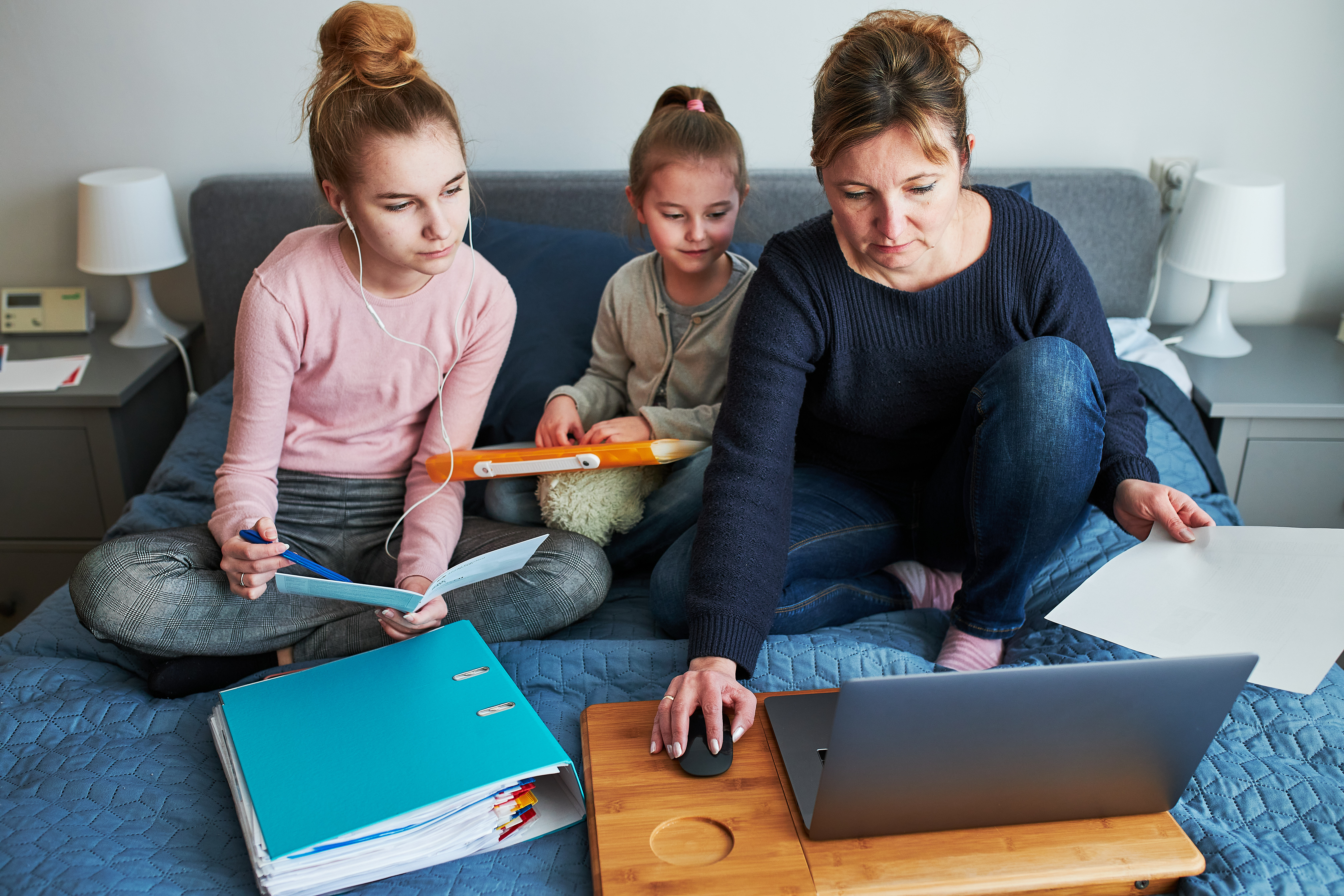 Women mother and daughter working learning remotely doing job homework during video chat call stream online course webinar lessons on laptop from home during COVID-19 quarantine. Women sitting on bed in front of computer looking at screen in company little girl playing around