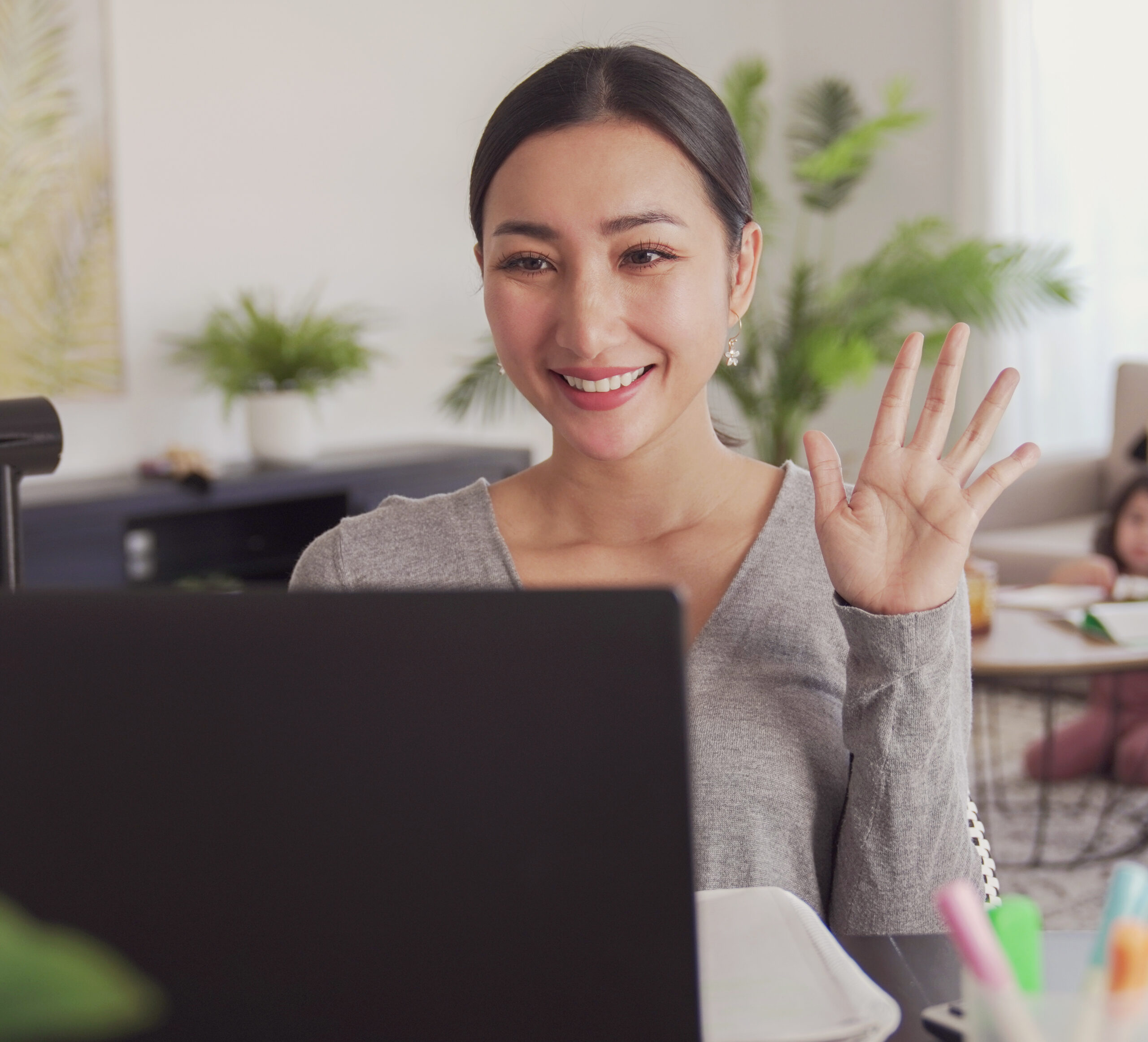 A young woman waves at a laptop she is using for virtual learning.