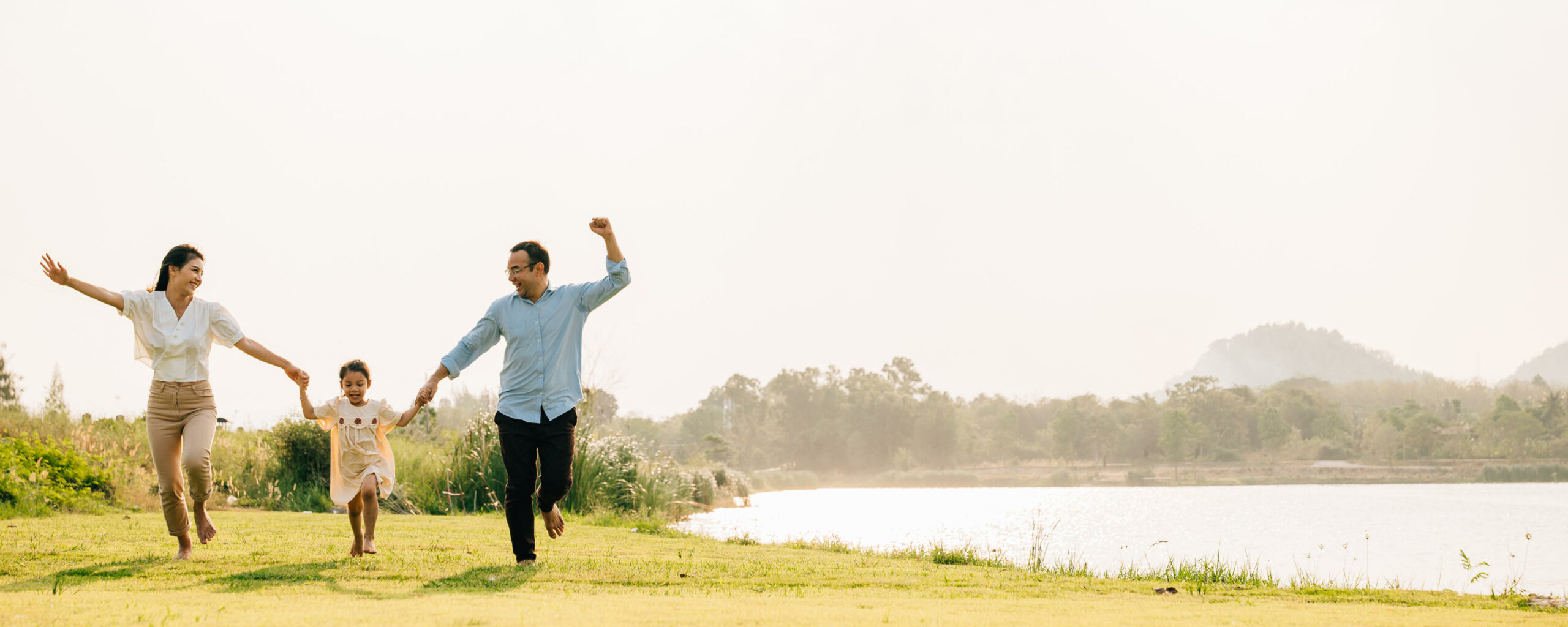 Asian family running and playing together in a beautiful nature setting, with a sunny sky and green grass all around, feeling carefree and happy, Happy Family Day Concept